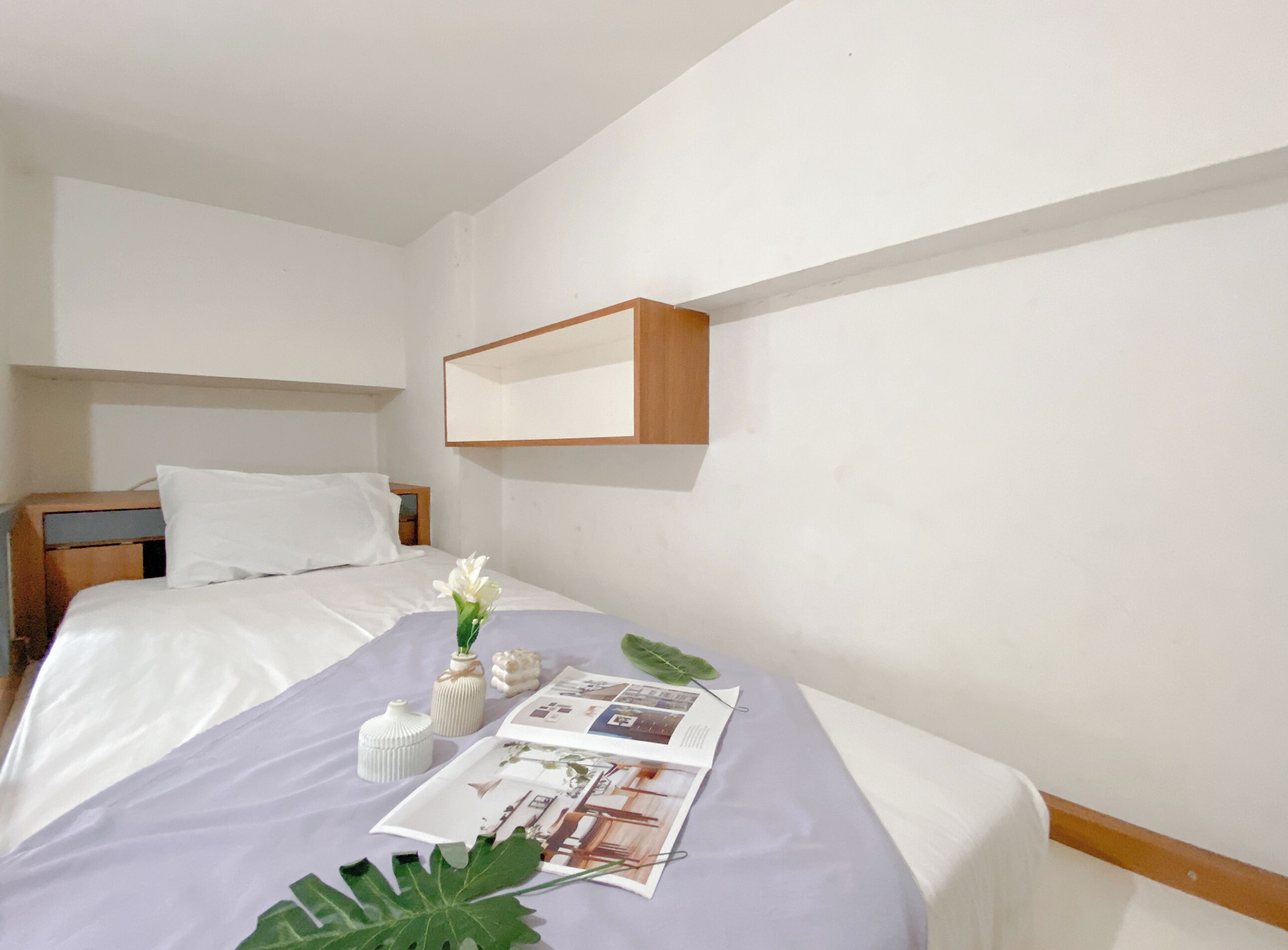 A hotel room with two beds, a wooden headboard, white bedding, a small table with a vase of flowers, and a magazine on the bed.