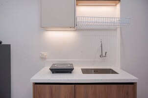 Uma cozinha moderna com um fogão por indução embutido, uma pia de aço inoxidável, armários de madeira e uma prateleira suspensa acima da pia.