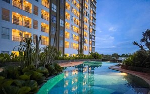 A multi-story hotel with a swimming pool surrounded by tropical plants. - Comfy 1BR Apartment at Tamansari Skylounge Makassar (Makassar)
