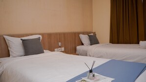 A hotel room with two beds, each with white bedding and a blue accent. There is a small table with a magazine and a reed diffuser. - Warm and Minimalist Studio (No Kitchen) at Great Western Apartment (Tangerang)