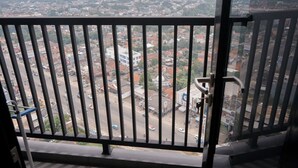 Un balcon doté d’une rambarde en métal, d’où l’on peut admirer un paysage urbain composé d’immeubles et de routes.