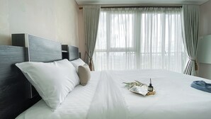 A hotel room with a large bed, a headboard, and a window with sheer curtains. - Cozy Studio Apartment at Casa De Parco near ICE BSD (Pagedangan)