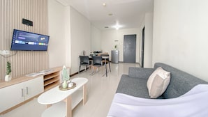 A modern living room with a flat-screen TV, a grey sofa, a white coffee table, and a dining area with chairs and a small table. - Fully Furnished and Comfortable 2BR Nifarro Park Apartment (Jakarta)