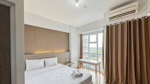 Une chambre d’hôtel avec un lit, une table de chevet sur laquelle se trouve une bouteille, une fenêtre avec des rideaux et un appareil de climatisation.