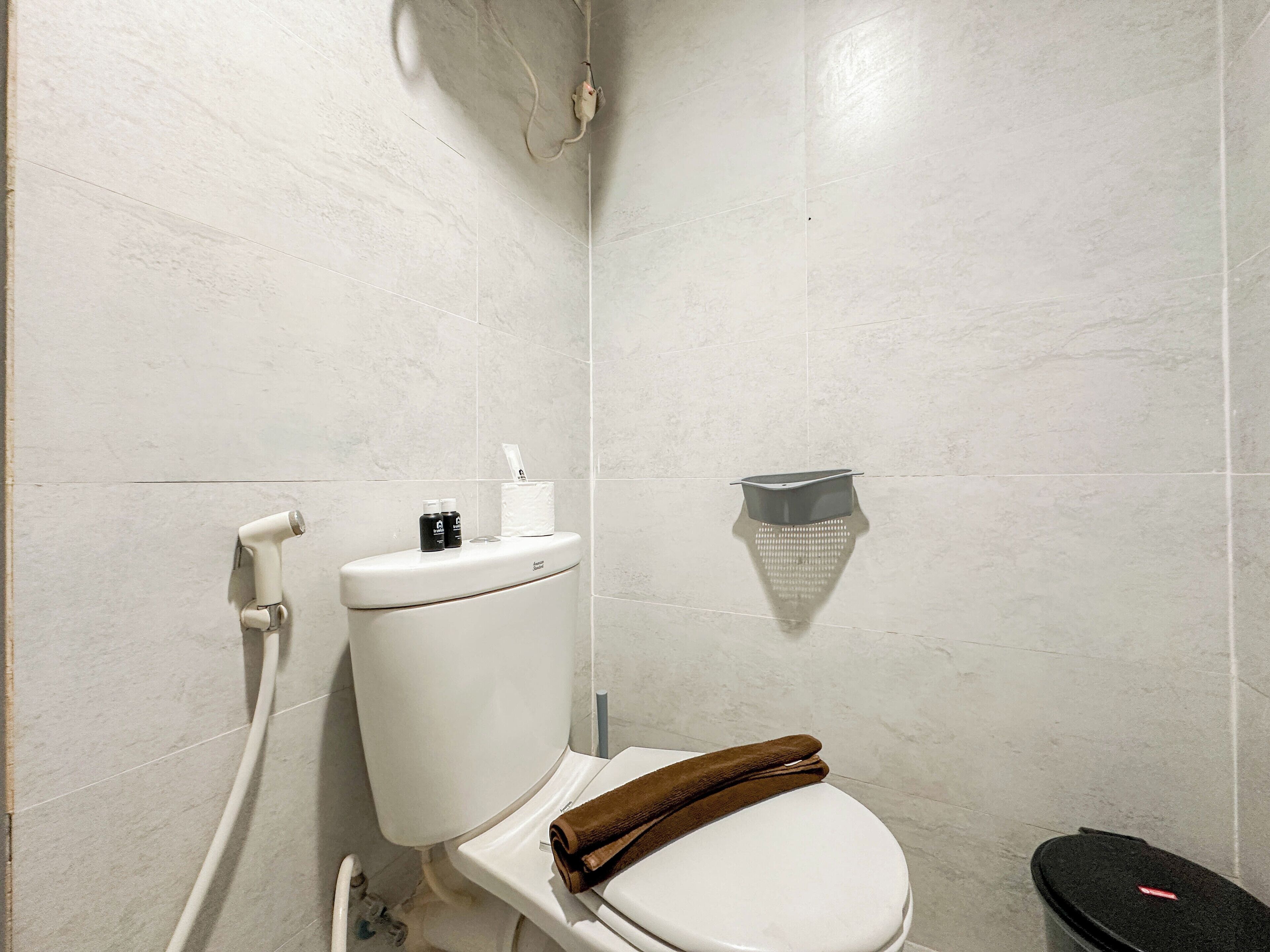 A bathroom with a toilet, a shower, and a trash bin.