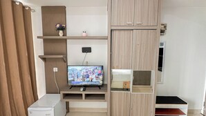 Un salon comprenant un téléviseur, un réfrigérateur blanc, un meuble en bois et une étagère ornée d’objets décoratifs.