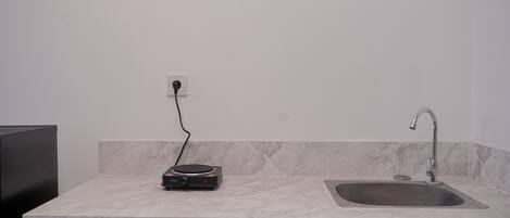A kitchen with a marble countertop, a sink, a black portable heater, and a power outlet.