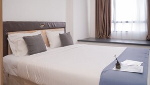 A neatly made bed with a headboard, pillows, and a bedside table with a lamp and papers. - Modern Style and Homey Studio Apartment Collins Boulevard (Tangerang)