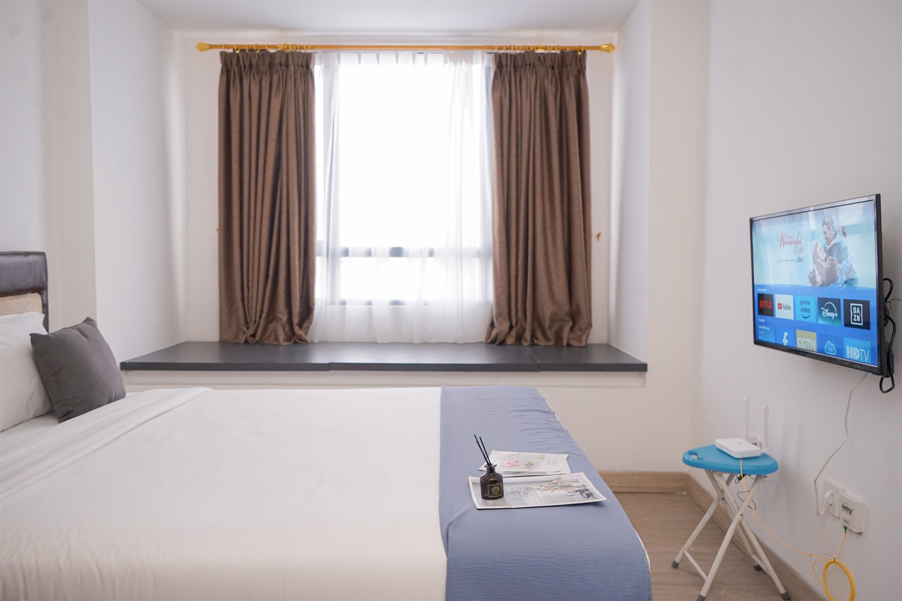 A hotel room with a bed, a window seat, a television, and a desk with a chair.