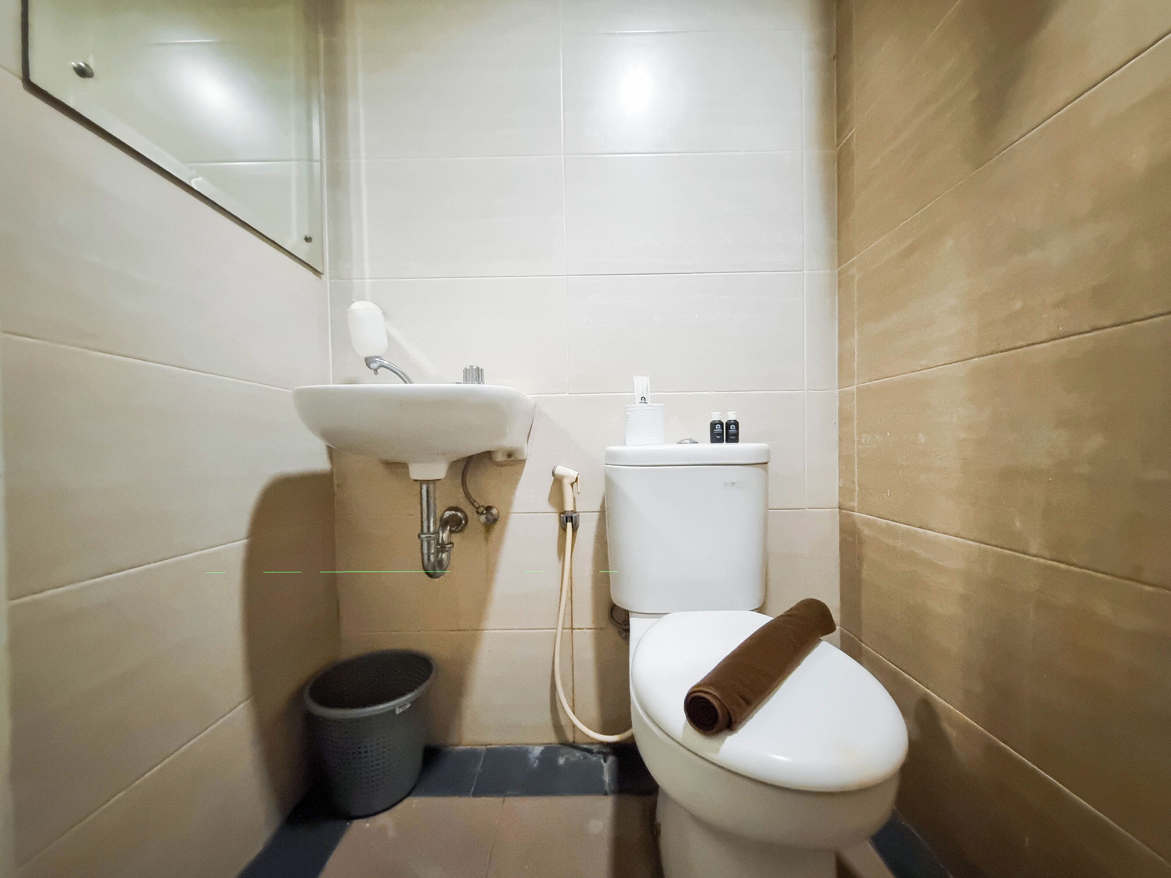 Un baño pequeño con lavamanos, inodoro y un cubo de basura blancos.