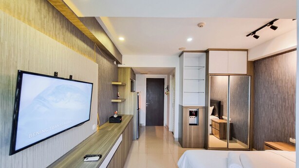 Una habitación de hotel moderna con un televisor de pantalla plana montado en la pared, un escritorio de madera, una cama con ropa blanca y un vestidor.