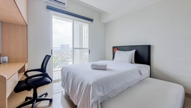 Habitación de hotel con cama, escritorio y silla. Se ve una ventana con vistas a edificios.
