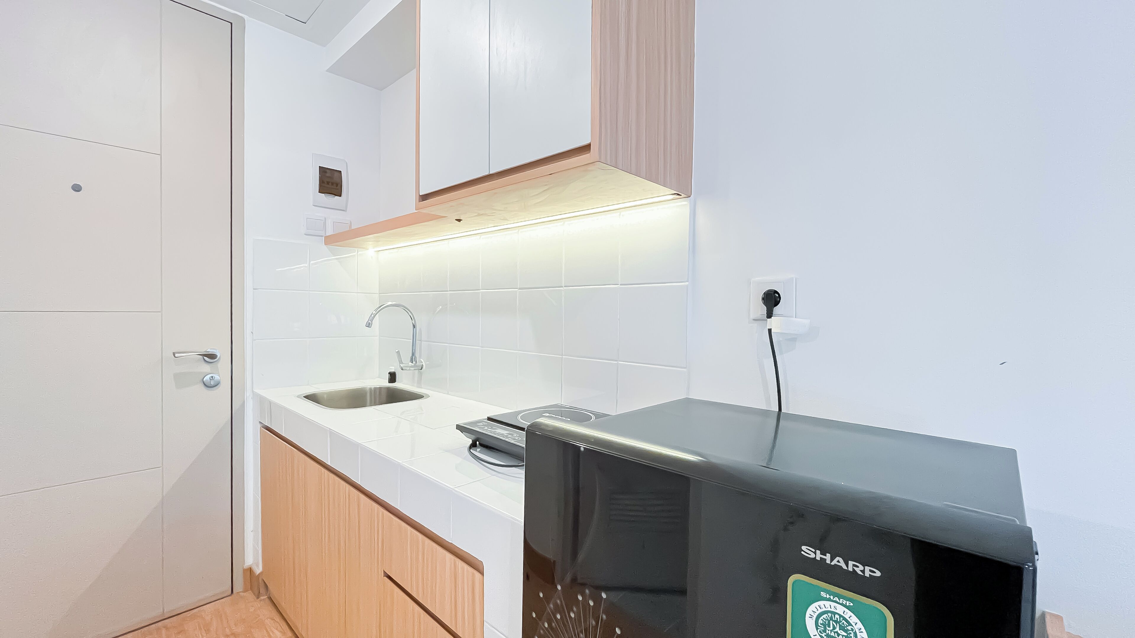 A modern kitchen with white tiles, a stainless steel sink, a built-in oven, and wooden cabinets.