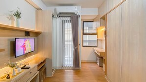 A modern, well-lit room with a flat-screen TV, wooden furniture, and a window with curtains.