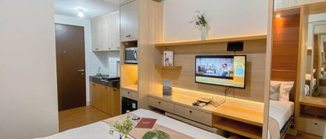 Una habitación de hotel con cama, mesita de noche, televisor y una pequeña kitchenette.
