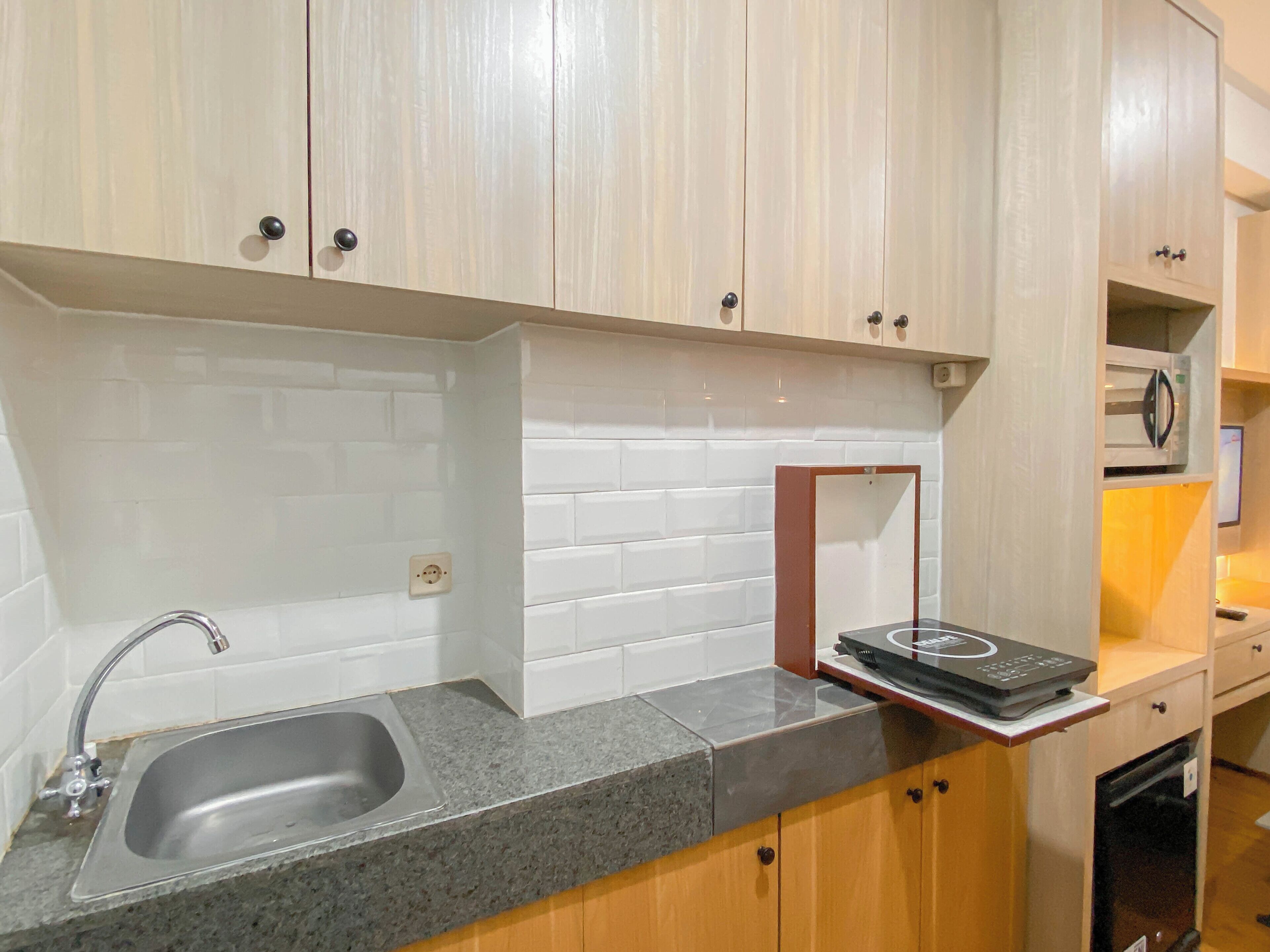 A kitchen with a granite countertop, a stainless steel sink, wooden cabinets, and a microwave on a shelf.