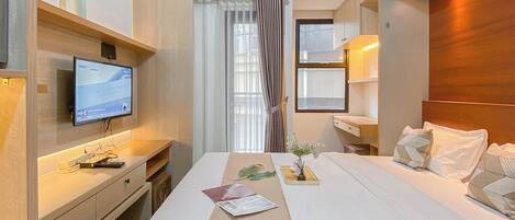 A hotel room with a bed, bedside table, TV, desk, and a window with curtains.