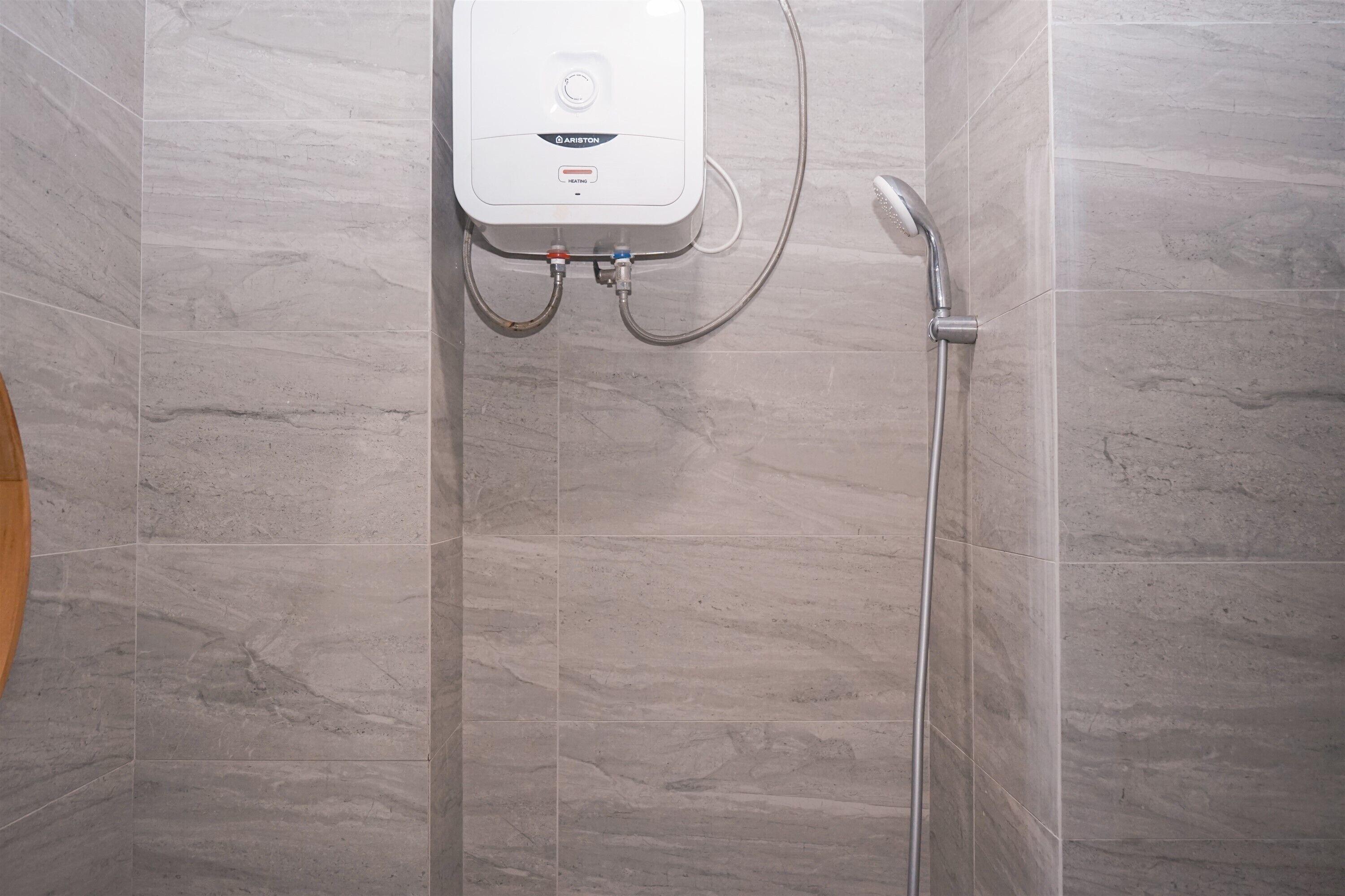 A bathroom with a shower, a wall-mounted water heater, and a wooden bath mat.