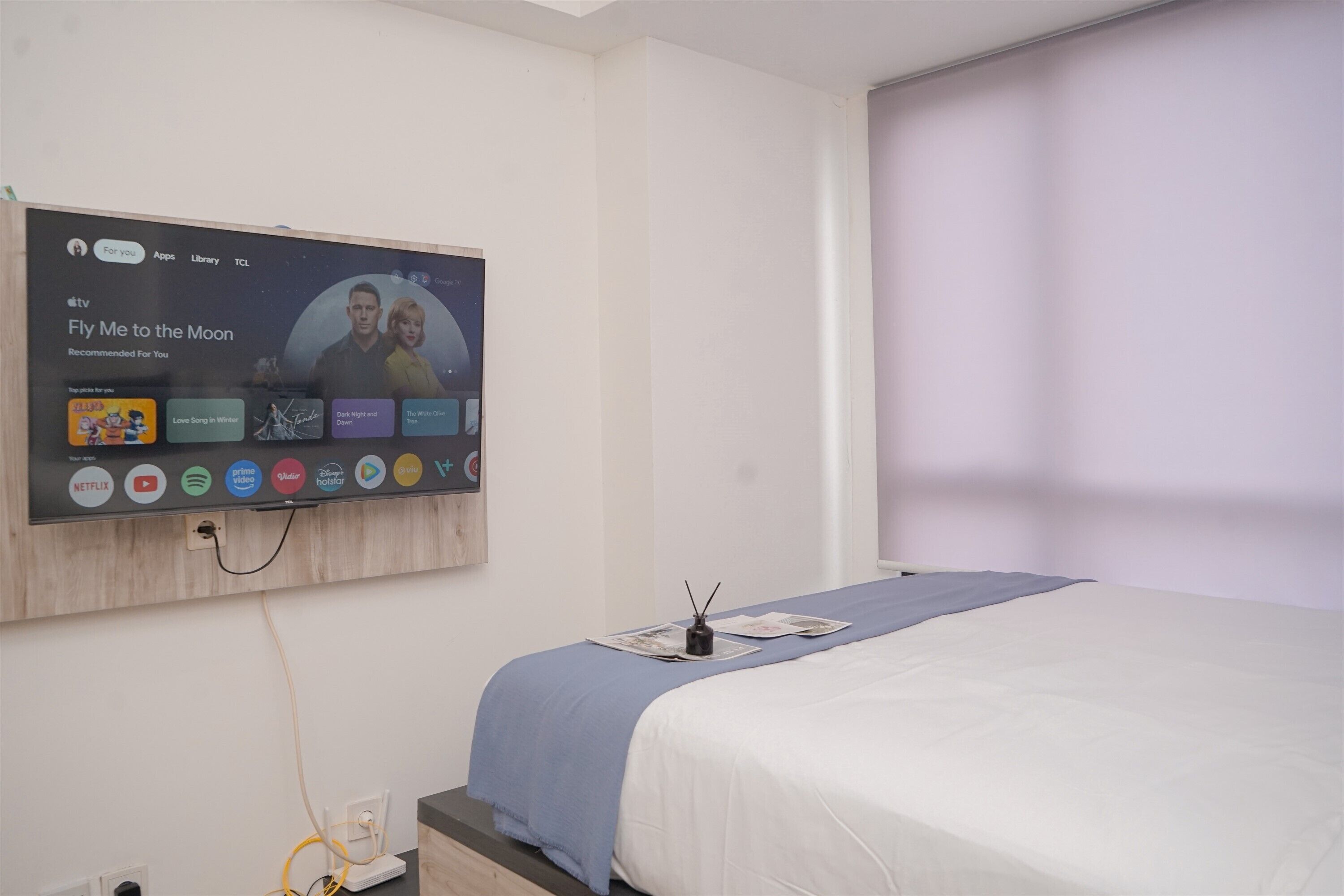 Een hotelkamer met een aan de muur bevestigde televisie die een film aanbeveelt.