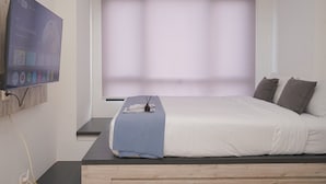 Une chambre à coucher avec un lit, un téléviseur fixé au mur et une fenêtre avec des stores.
