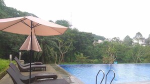 A poolside area with lounge chairs and an umbrella, surrounded by lush greenery and a view of a residential area. - Cozy 1BR without Living Room at Royal Heights Apartment (Bogor)