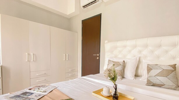 A hotel room with a bed, a wooden tray with decorative items, a magazine, and a plant. - Cozy 1BR without Living Room at Royal Heights Apartment (Bogor)