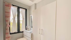 A room with a white wardrobe, a small white desk, and a window with floral curtains. - Cozy 1BR without Living Room at Royal Heights Apartment (Bogor)
