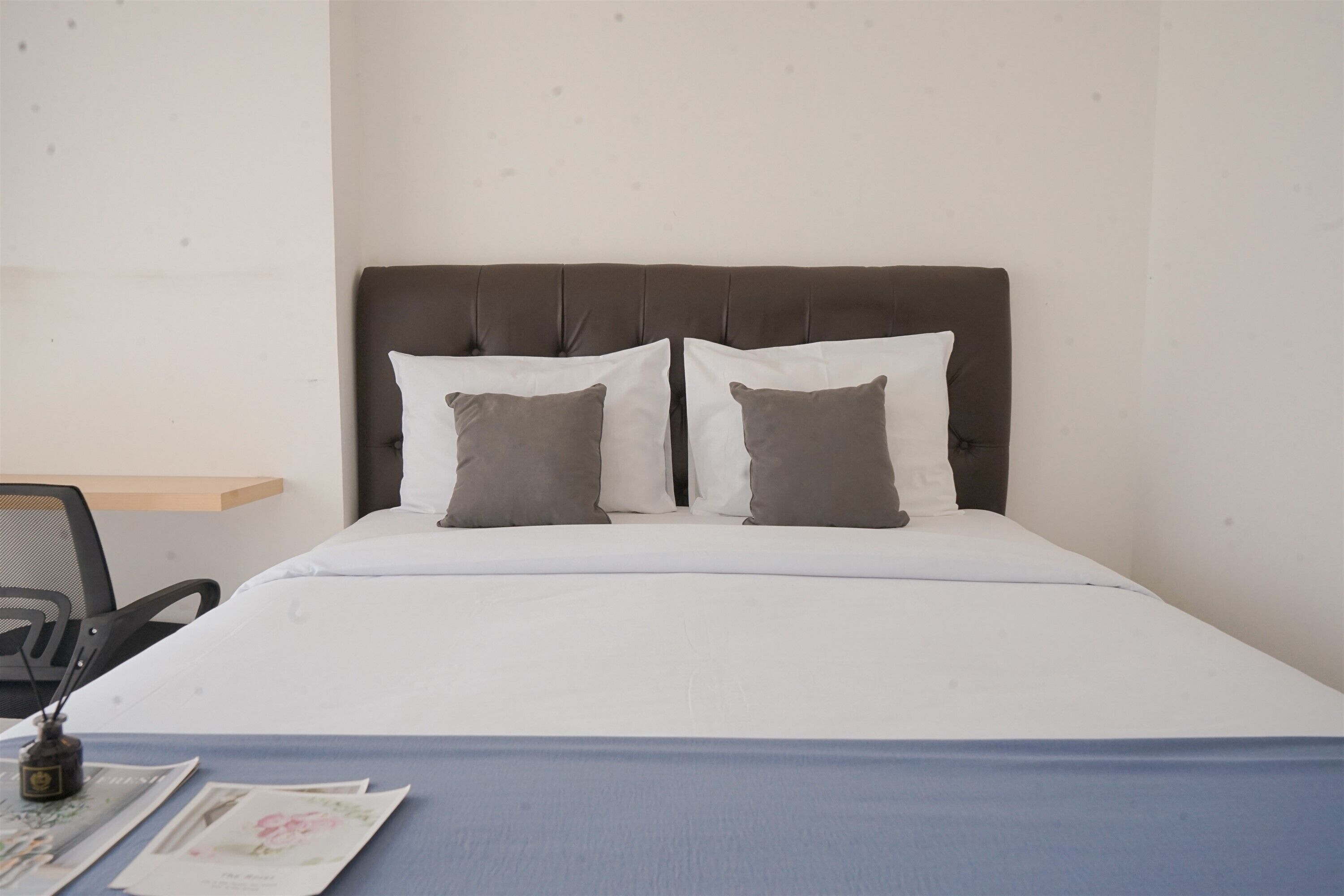 A neatly made bed with a dark headboard, two pillows, and a blue bedspread.