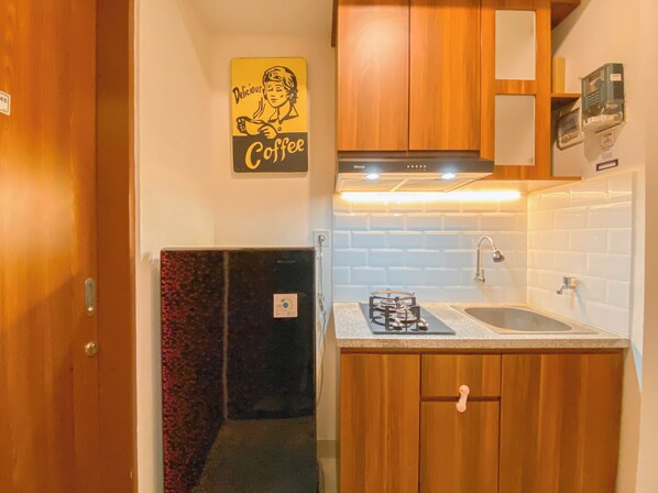 A compact kitchen with wooden cabinets, a gas stove, a sink, and a wall-mounted oven. - Homey 1BR without Living Room at Grand Kamala Lagoon Apartment (Bekasi)