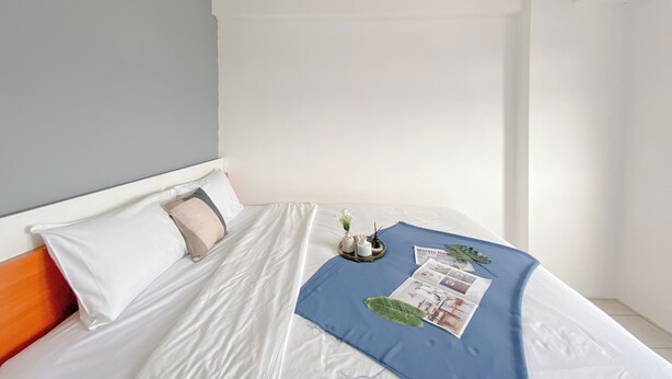A neatly made bed with white linens, a blue blanket, and a magazine. - Comfy 1BR Apartment with Extra Room at Green Pramuka City near Mall (Jakarta)