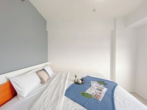 A neatly made bed with white linens, a blue blanket, and a magazine. - Comfy 1BR Apartment with Extra Room at Green Pramuka City near Mall (Jakarta)