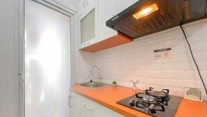 A kitchen with white cabinets, an orange countertop, a gas stove, a sink, and a window with blinds. - Comfy 1BR Apartment with Extra Room at Green Pramuka City near Mall (Jakarta)