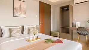 Ein Hotelzimmer mit einem ordentlich bezogenen Bett, einem Stadtbild an der Wand, einem Kleiderschrank, einem Schreibtisch mit Stuhl und einer Klimaanlage.