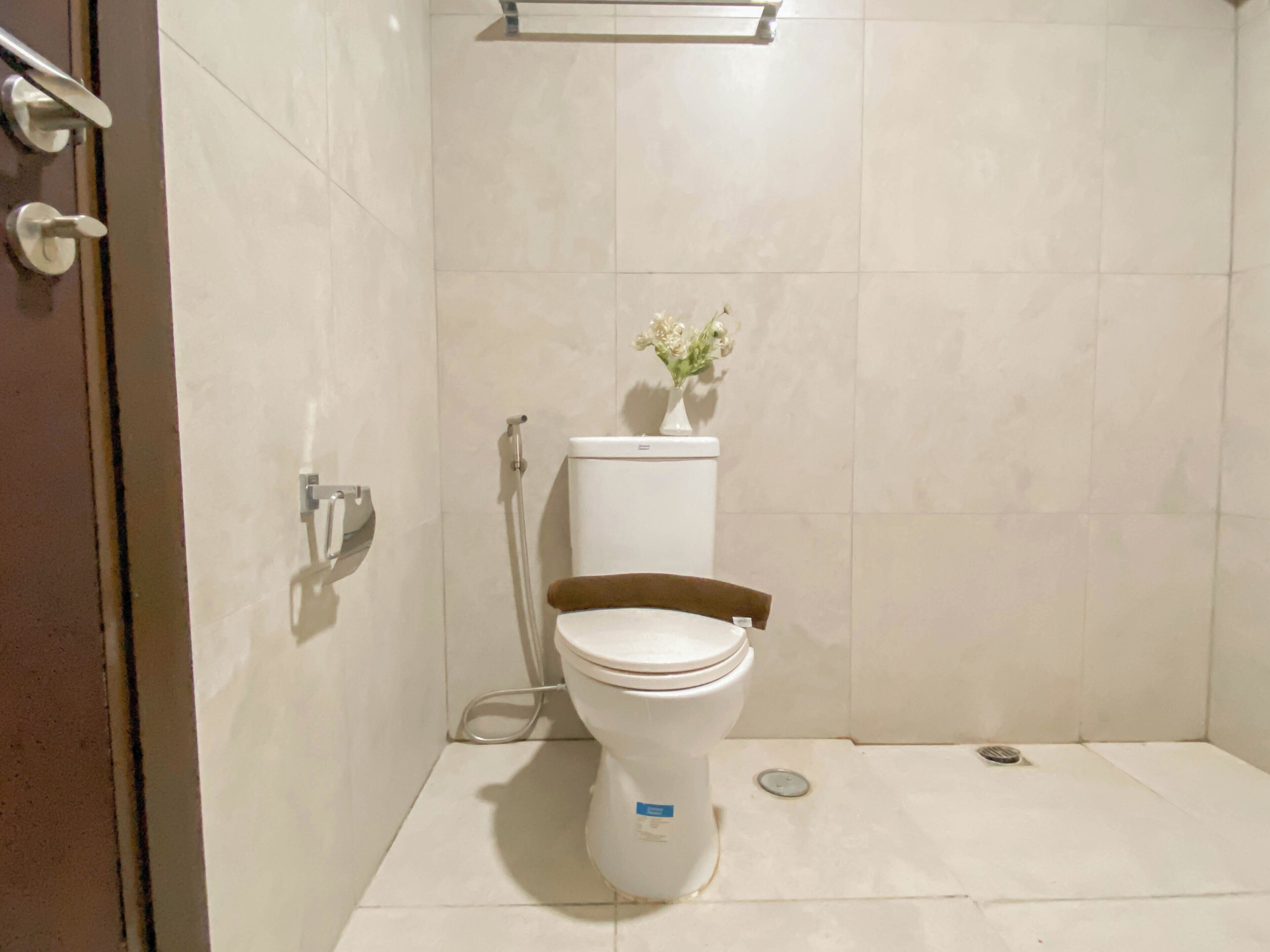 A bathroom with a toilet, a shower, and a small flower vase on the wall.