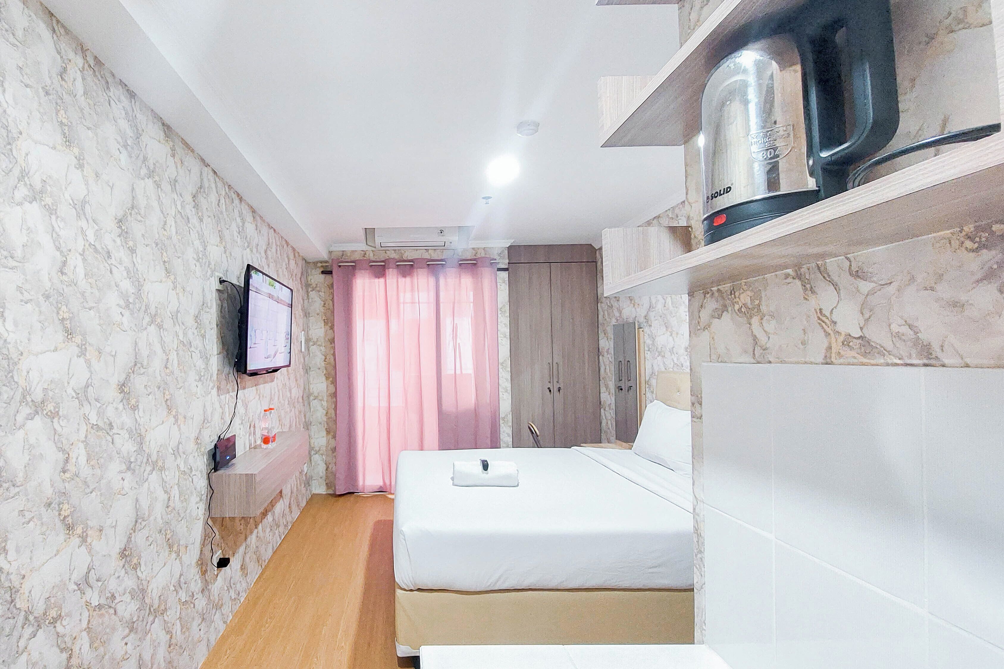 A hotel room with a bed, a TV mounted on the wall, a kettle, and a shelf with a kettle.