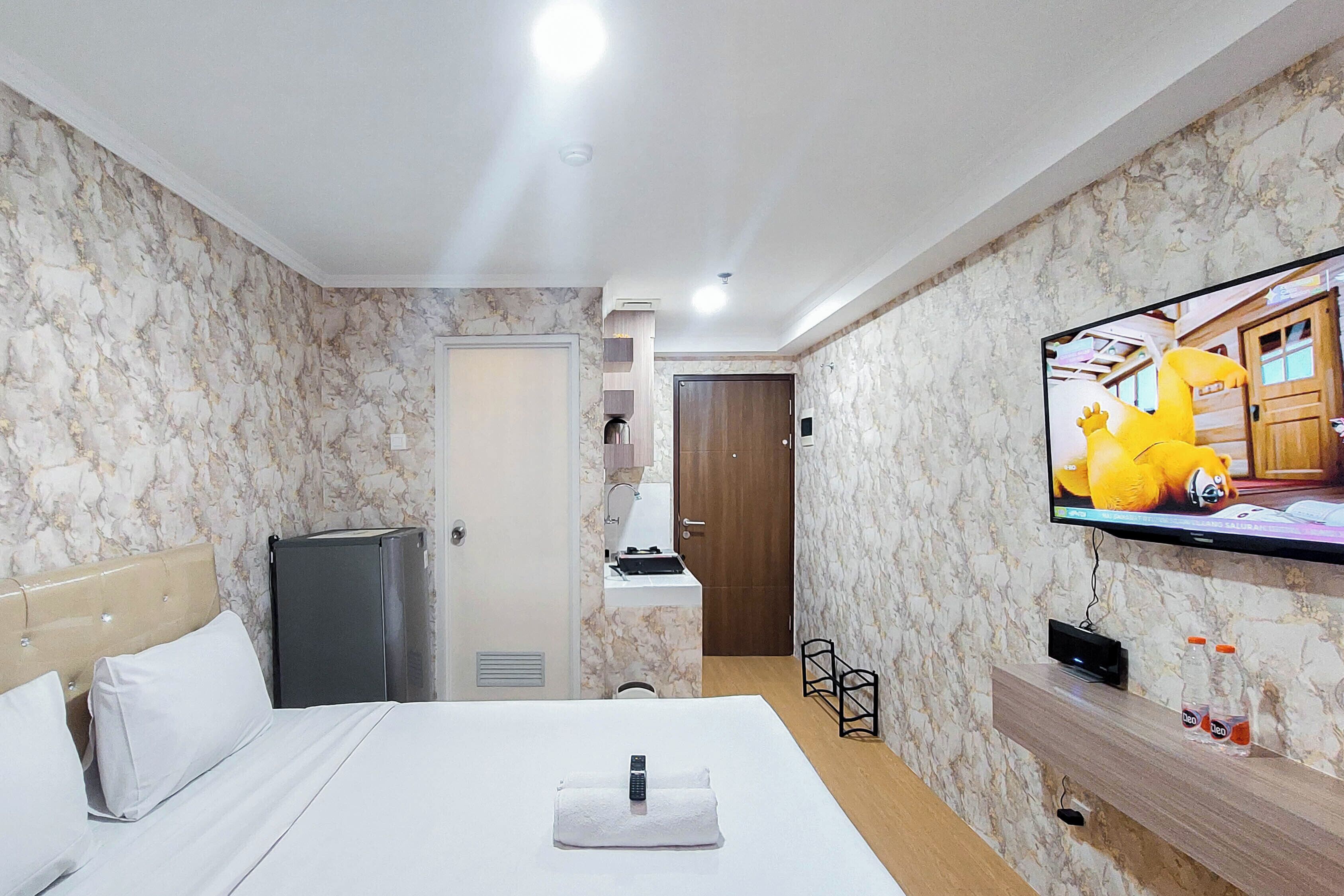 A hotel room with a bed, a TV, a minibar, and a bathroom.