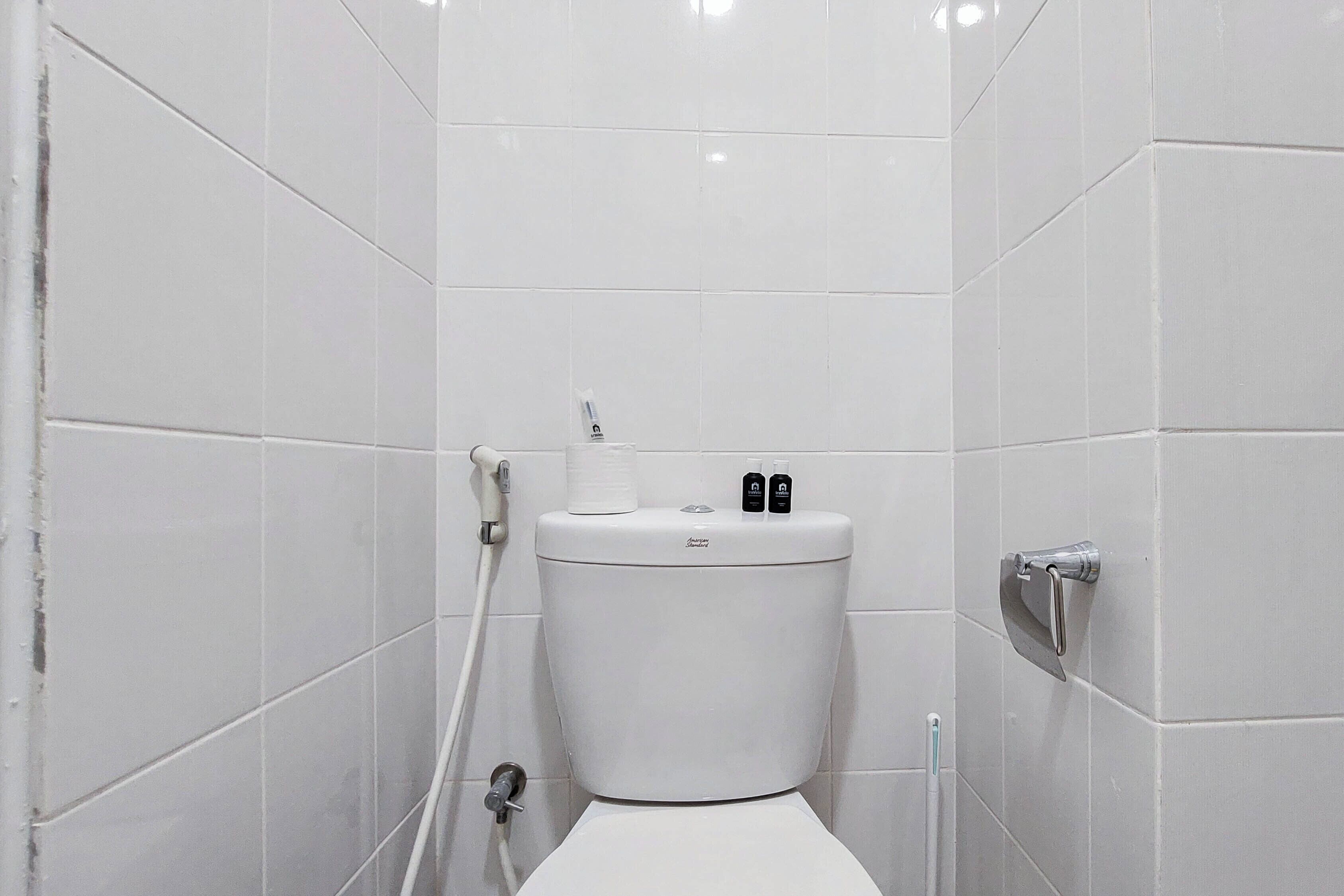 A small, white-tiled bathroom with a toilet, a hand dryer, and a faucet.