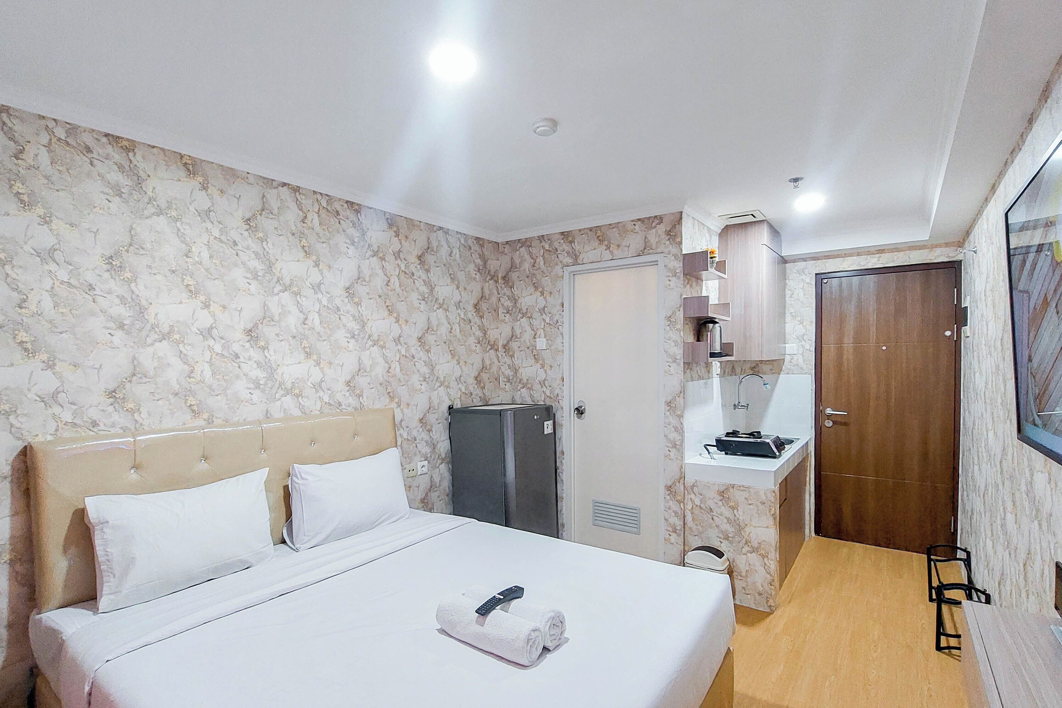 A hotel room with a bed, a minibar, a door, and a small table.