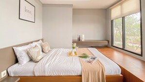 A modern bedroom with a large bed, a bedside table, a nightstand, a window with a view, and a framed picture on the wall. - Simply Look And Best Deal 2BR at Pollux Chadstone Apartment (Cikarang)