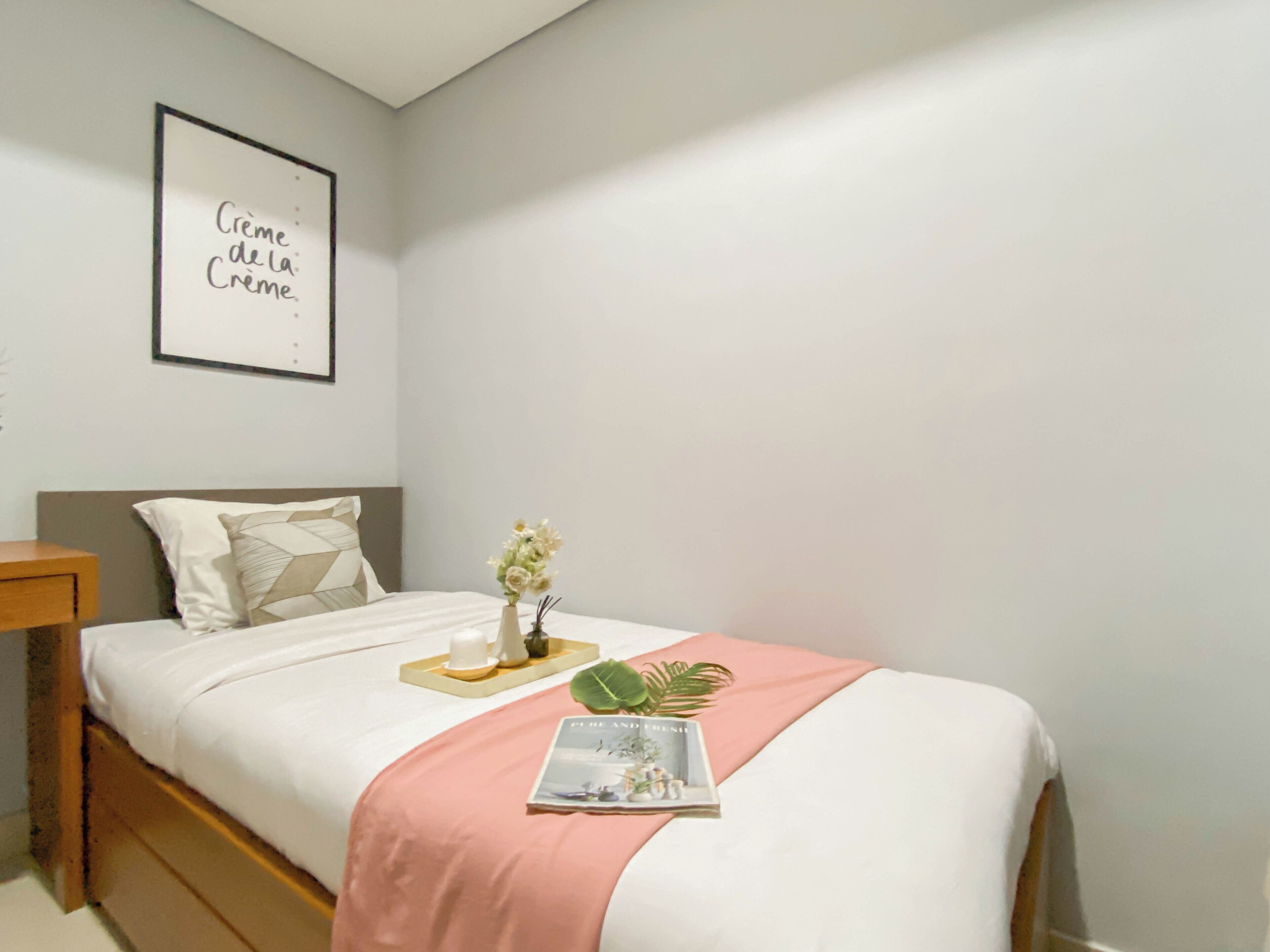 Ein ordentlich bezogenes Bett mit einer rosa Decke, einer Vase mit Blumen und einer Zeitschrift auf dem Bett.