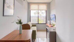 A modern living room with a sofa, a wooden table, a TV, and a window with blinds. - Simply Look And Best Deal 2BR at Pollux Chadstone Apartment (Cikarang)