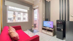 A compact living space with a red sofa, a small table with a vase, a television, and a refrigerator. - Spacious 1BR at Grand Asia Afrika Apartment (Bandung)