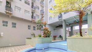 A residential building with a swimming pool, balconies, and potted plants. - Spacious 1BR at Grand Asia Afrika Apartment (Bandung)