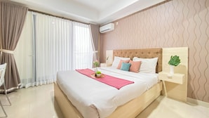 A modern hotel room with a large bed, a bedside table with a lamp, and a view of the outside through sheer curtains. - Homey Studio Apartment at Beverly Dago (Bandung)