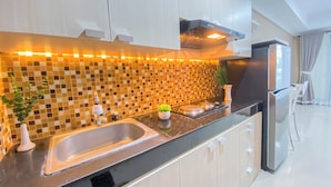 A modern kitchen with a black countertop, a sink, and a stove. There is a tiled backsplash and a plant on the counter. - Homey Studio Apartment at Beverly Dago (Bandung)