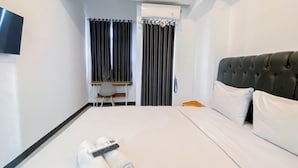 Habitación de hotel con cama, escritorio, silla, televisor y puerta con cortinas.