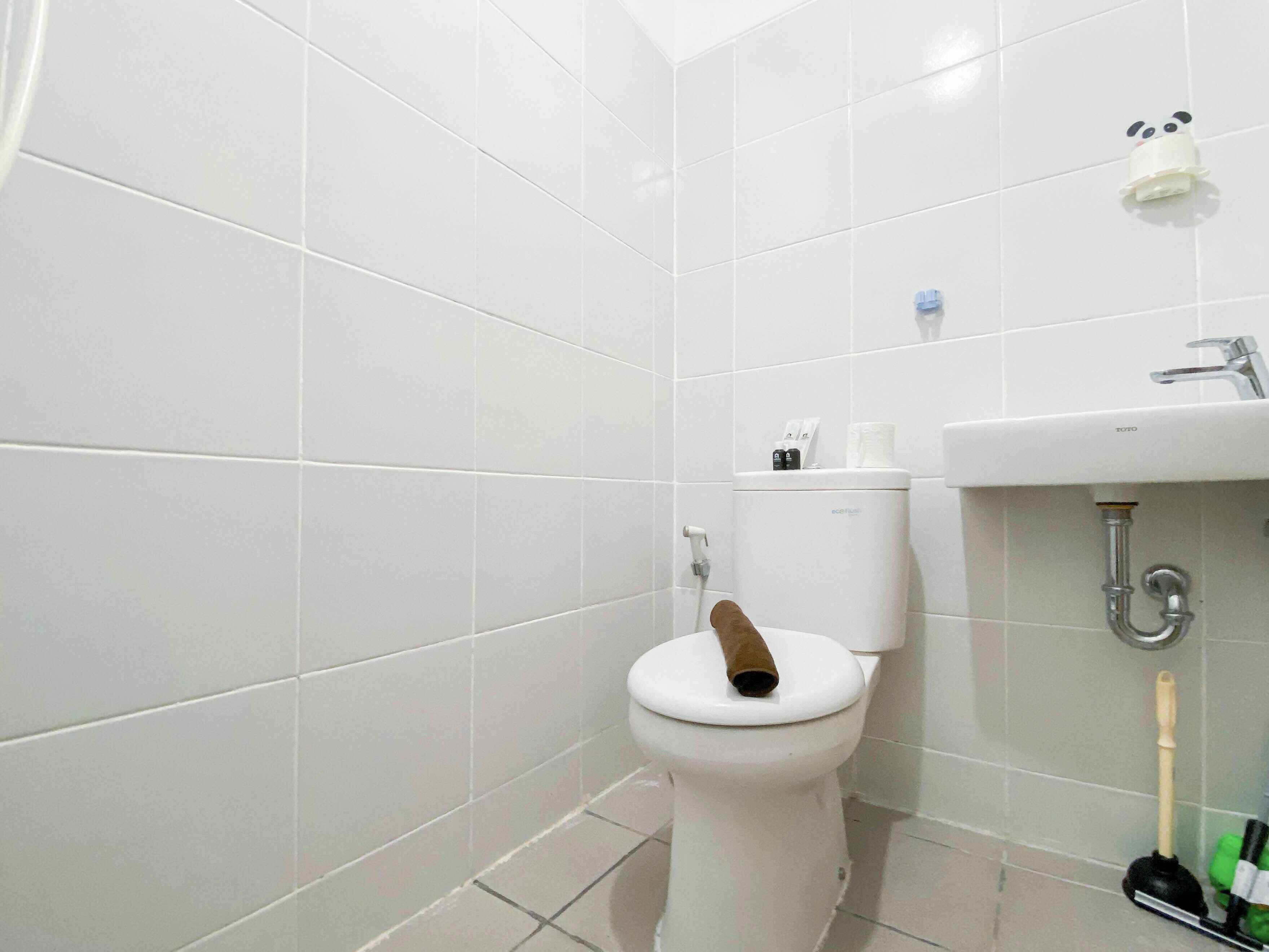 A bathroom with white tiles, a toilet, a sink, and a toilet brush.
