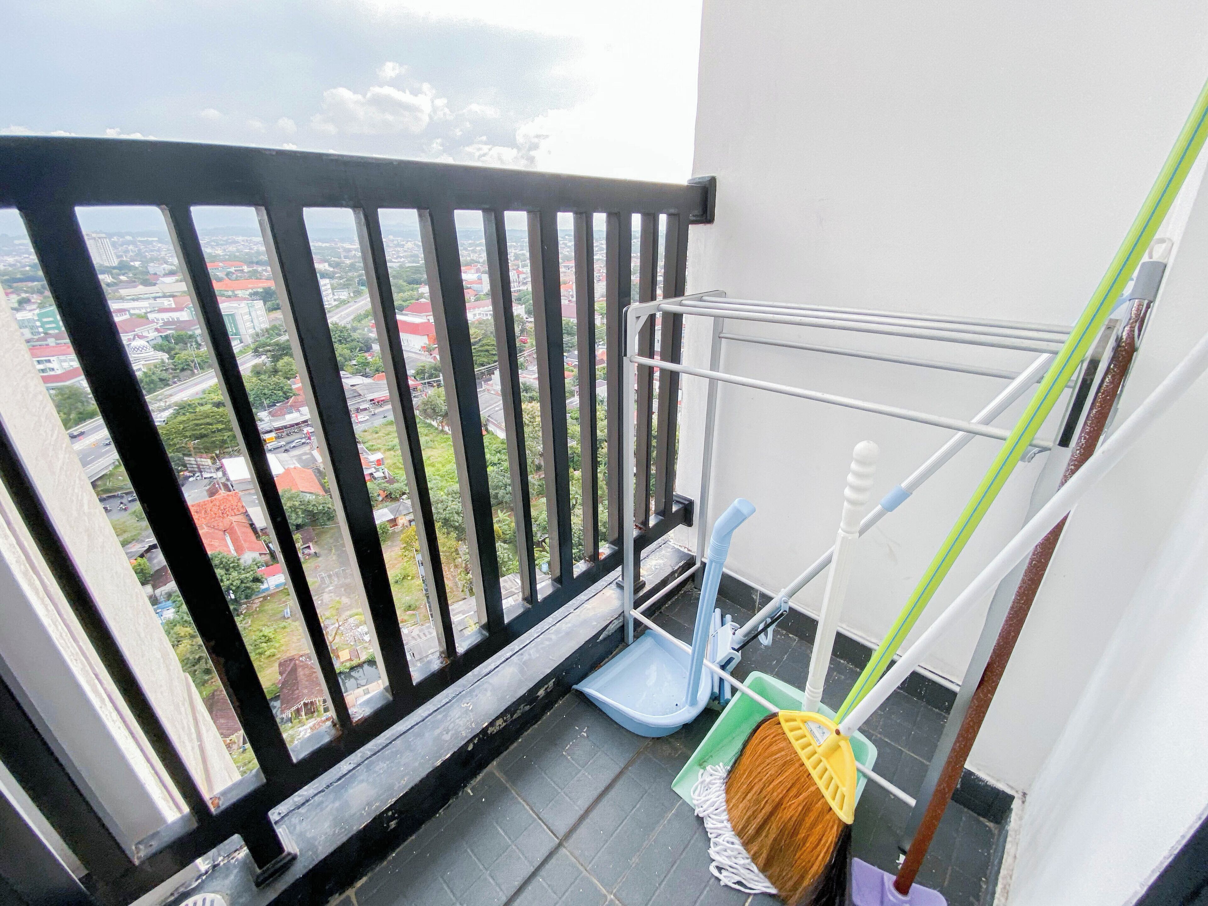 A balcony with a view of a cityscape, a mop, and a broom leaning against a metal rack.