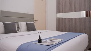 A neatly made bed with a blue blanket, a small black vase with reeds, and a newspaper.