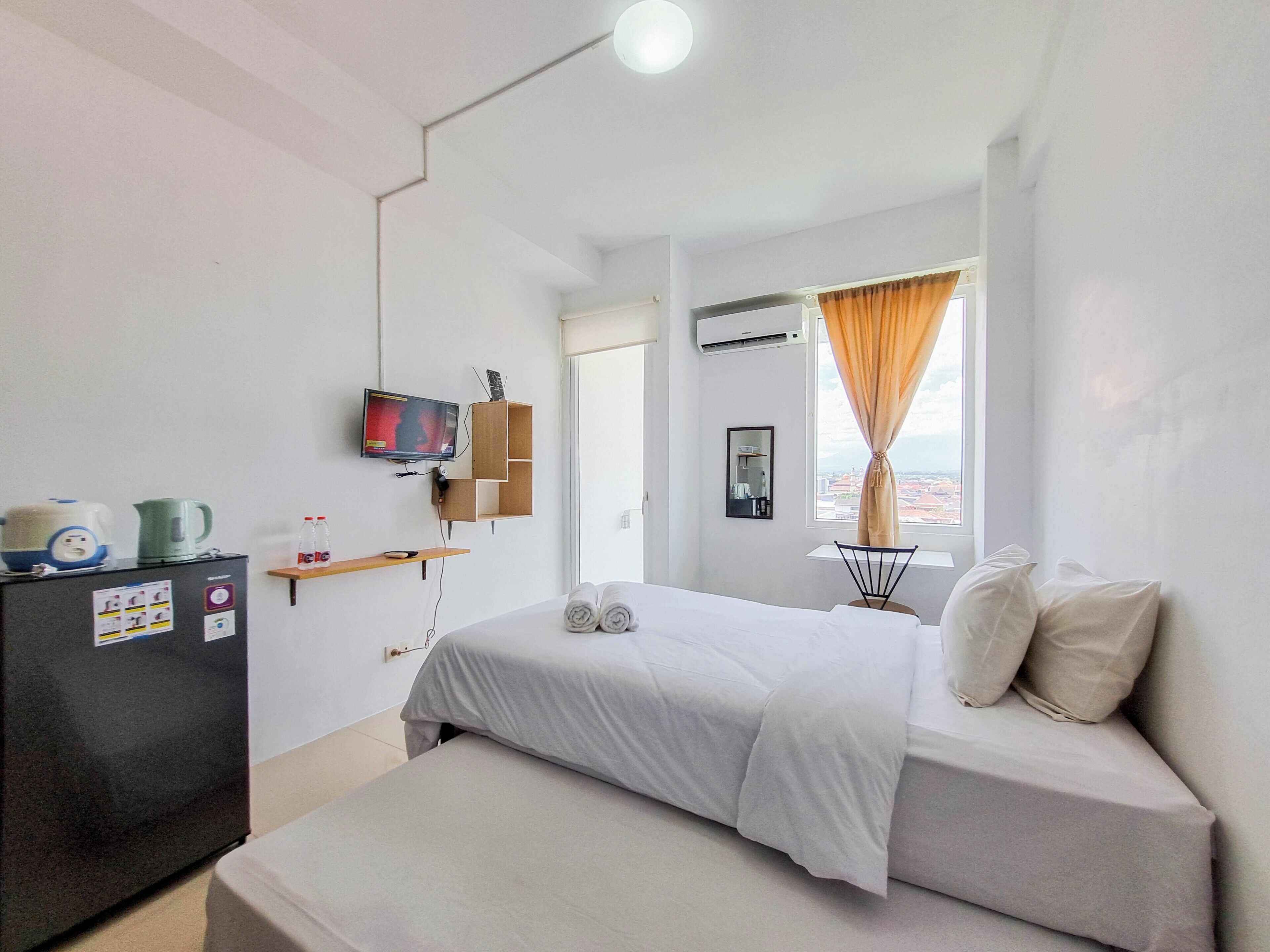 A hotel room with a bed, a TV, a small kitchenette, and a window with curtains.